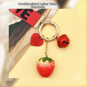 Detail of red strawberry keychain with love ribbon and metallic bell accessory