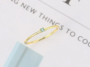 Macro shot of a minimalist gold ring featuring a four-prong set round light blue zircon stone