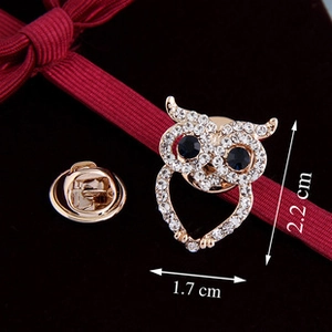 Macro shot of owl brooch with crystals and dimensions of 1.7cm by 2.2cm on red velvet