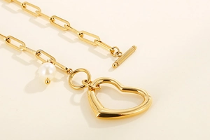 Detail of gold paperclip chain necklace with heart pendant, pearl and OT toggle clasp