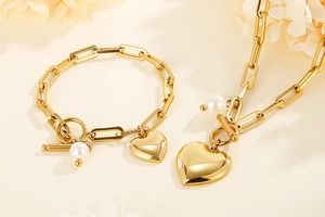 Détail de la chaîne trombone dorée et du bracelet avec breloques cœur et perle d'eau