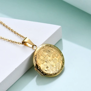 Detailed view of a round gold locket pendant with intricate floral relief on a white stand