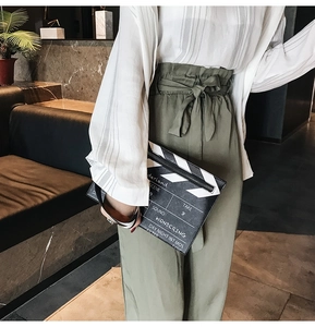 Close-up of a trendy clapperboard-shaped crossbody bag styled with olive green trousers