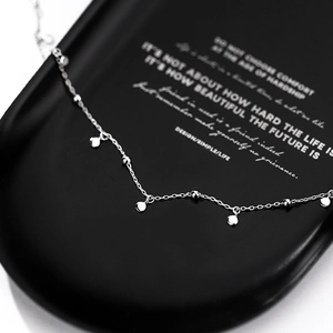 Minimalist silver choker necklace with polished metal discs and round beads on black stand