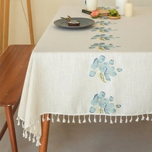 Detailed embroidery of blue floral patterns on beige linen tablecloth with tassels