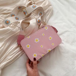 Pink floral shoulder bag with daisy embroidery and wide strap on yellow dress background
