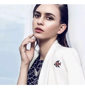 Detail of a fish-shaped brooch with colorful rhinestones on a white blazer collar