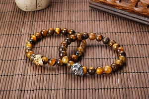 Detail of tiger eye bead bracelets with gold and silver skull charms on bamboo mat