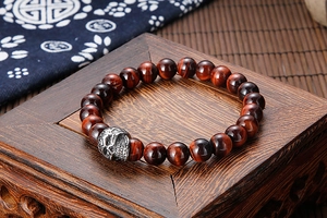 Macro detail of red tiger eye beads and vintage skull charm on a wood stand