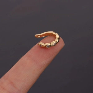 Close-up of a small gold U-shaped ear cuff with clear zircons held on a fingertip