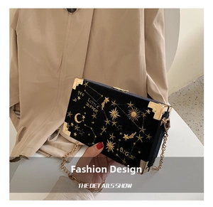 Detail of black velvet box bag featuring gold star and moon embroidery with chain strap