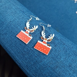 Detail of Christmas reindeer earrings popping out of a red gift box on a blue background