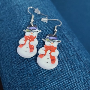 Close-up of cute snowman acrylic earrings featuring black hats and red scarves