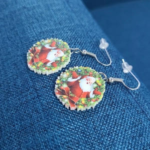 Close-up of Santa Claus in wreath acrylic Christmas earrings on blue background