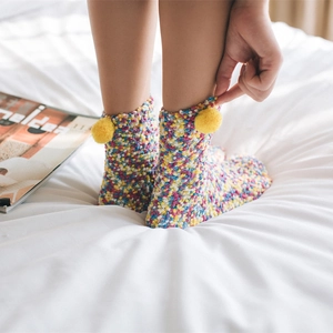 Colorful coral fleece cake socks with yellow pom-poms on a soft white bed background