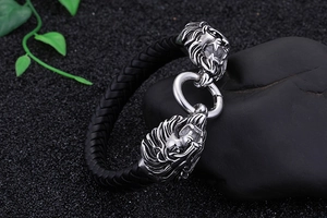 Nahaufnahme von Herren-Lederarmband mit Doppel-Löwenköpfen aus Stahl auf dunklem Sand