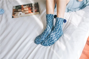 Blue coral fleece home socks with soft pom-poms on cozy white bedding detail
