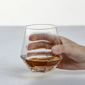 Close-up of hand holding a diamond-cut glass filled with amber liquid for whisky or juice