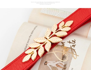 Close-up of a red skinny belt featuring a golden leaf buckle on an open book background