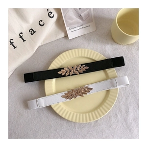Close-up of golden leaf metal buckle and elastic fabric texture on black and white waist belts