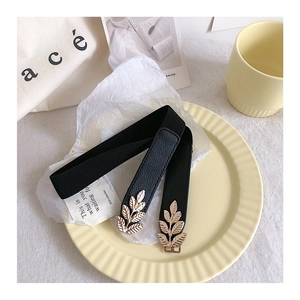 Close-up of black elastic belt featuring a golden leaf metal buckle on a stylized tray
