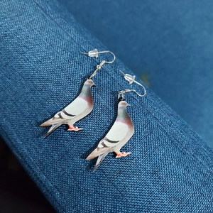 Close-up of acrylic pigeon drop earrings with silver hooks on blue textured fabric