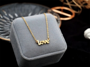 Detailed close-up of golden Love letter pendant with heart-shaped O on velvet box