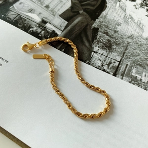 Detail of a minimalist gold twisted rope bracelet featuring a polished lobster clasp