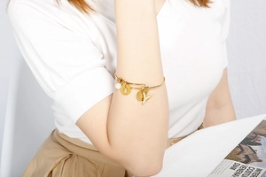 Detail of gold stainless steel bangle featuring letter Y charm and white bead on wrist