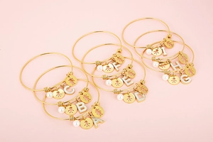 Detail view of gold stainless steel bangle with letter charms and pearl decorations