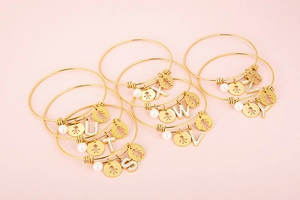 Detail of gold letter charms and white pearls on stainless steel bangle bracelets