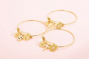 Detail of gold open bracelets with pearl charms and alphabet letter pendants