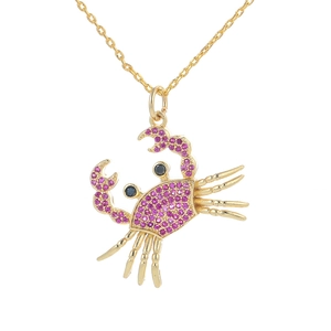 Macro detail of gold crab pendant necklace featuring pink pavé crystals on white backdrop