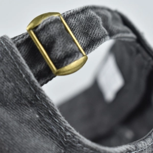 Detailed close-up of dark gray washed cotton baseball cap with adjustable bronze metal buckle