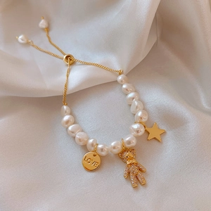 Detail of baroque pearl bracelet with gold teddy bear pendant and LOVE charm on satin