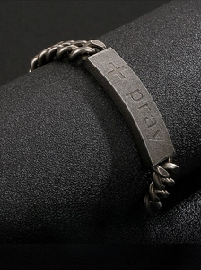 Macro shot of vintage steel cuban link bracelet with 'pray' cross engraving