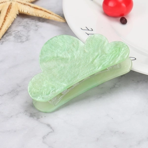 Macro view of a shimmering green cloud-shaped hair claw with glossy marble texture