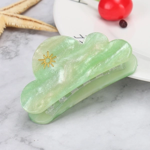 Detail of green cloud hair claw clip with marble texture and golden sun motif