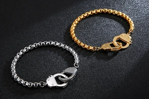 Detailed view of silver and gold handcuff-shaped bracelets on a black textured background