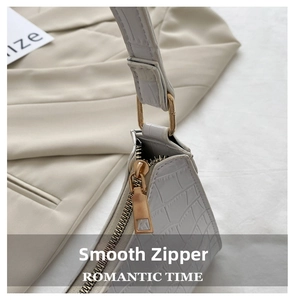 Detail view of smooth metal zipper and white crocodile embossed texture on shoulder bag