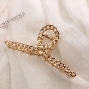 Detail shot of golden metal hair claw with chain texture on white fabric background