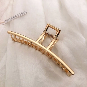Detailed view of a large golden metal hair claw clip with a strong spring on white fabric
