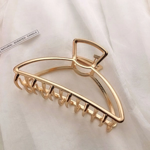 Detailed view of glossy gold metal hair claw clip on soft white fabric background
