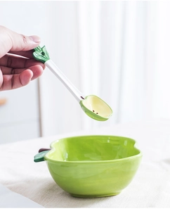 Close-up of green apple-shaped ceramic salad bowl with matching spoon in hand