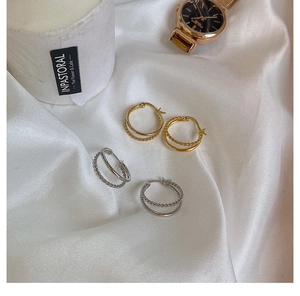 Detail of gold and silver double-layered twist hoop earrings on white silk fabric