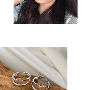 Detail of silver double hoop earrings with twisted and smooth texture on wooden base