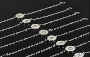 Détail de bracelets en acier inoxydable avec breloques rondes en nacre et lettres de A à H