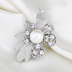 Detail showing crystal flower brooch with pearl center on elegant white silk background