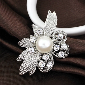 Close-up of a silver flower brooch with central pearl and rhinestone petals on silk