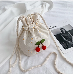 Close-up of canvas bucket bag with daisy embroidery and plush cherry charm details
